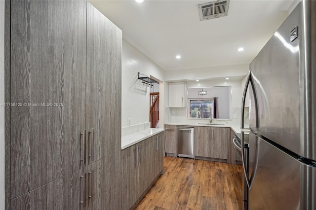 kitchen with modern cabinets, stainless steel appliances, visible vents, light countertops, and dark wood finished floors