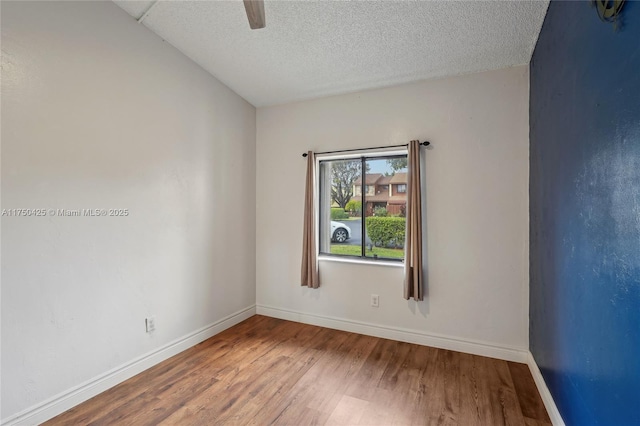 empty room with a textured ceiling, wood finished floors, ceiling fan, and baseboards