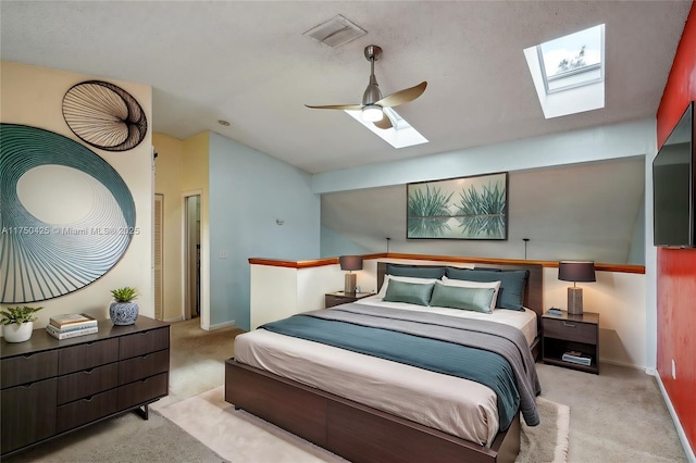 bedroom featuring vaulted ceiling with skylight, carpet flooring, baseboards, visible vents, and a ceiling fan