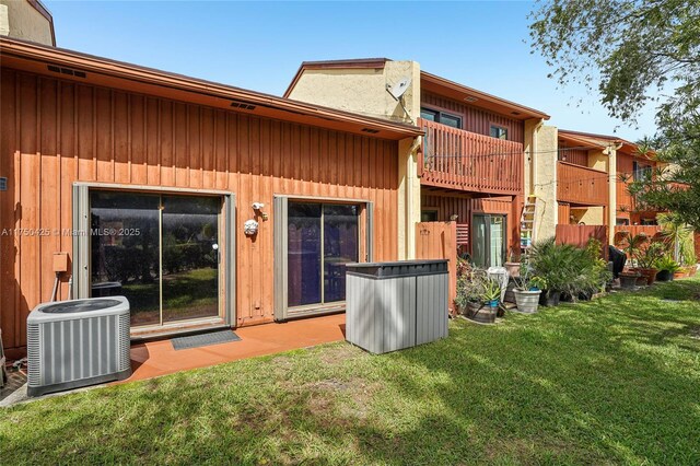back of house with a lawn, a chimney, central AC, and a balcony