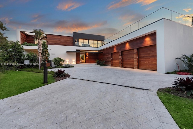 modern home with a garage, a front lawn, decorative driveway, and stucco siding