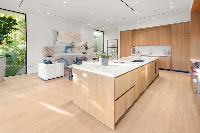 kitchen with a center island with sink, modern cabinets, light countertops, floor to ceiling windows, and a sink