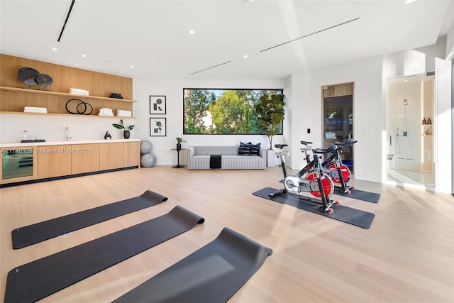 exercise area with wine cooler, light wood-style flooring, and recessed lighting