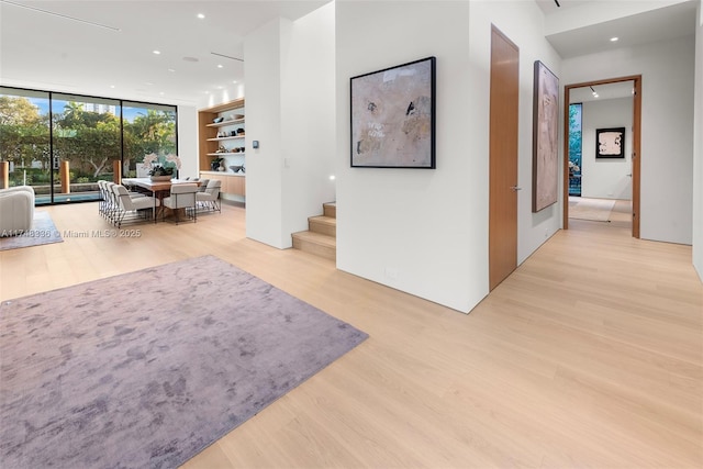 hallway with light wood-type flooring, stairs, floor to ceiling windows, and recessed lighting