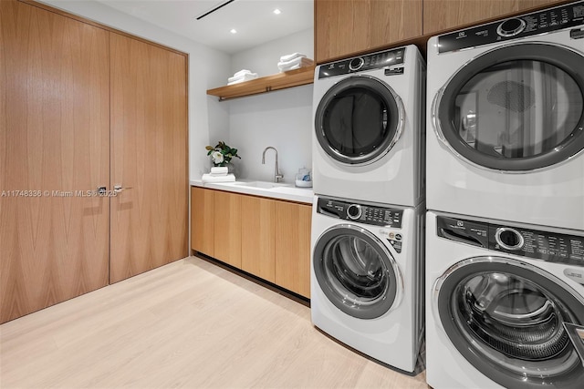 laundry room featuring stacked washer and dryer, a sink, cabinet space, and light wood-style floors