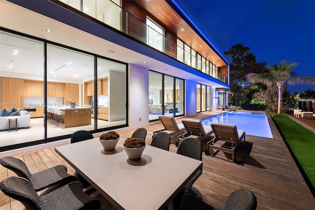 pool at twilight featuring outdoor dining area, an outdoor bar, an outdoor pool, and a deck