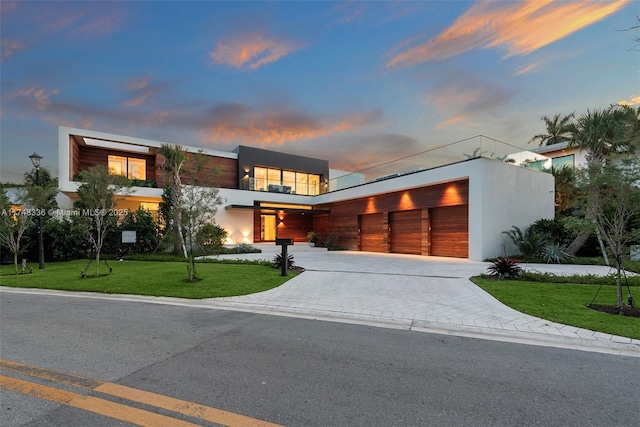 contemporary home with a garage, decorative driveway, a lawn, and stucco siding