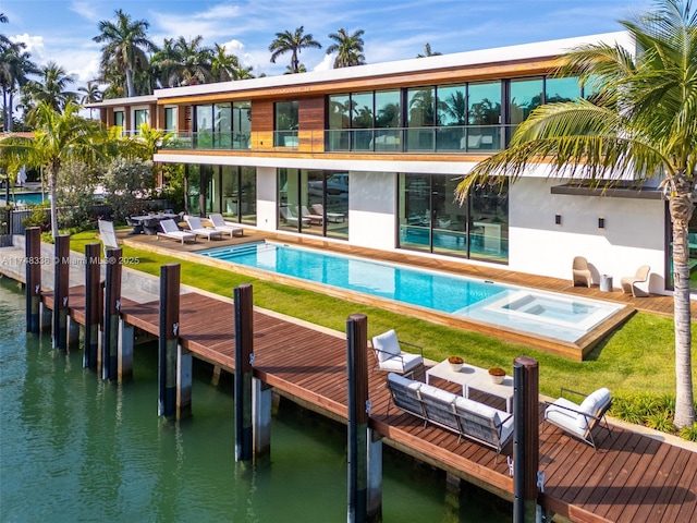 rear view of property with a yard, a water view, an outdoor pool, and an in ground hot tub