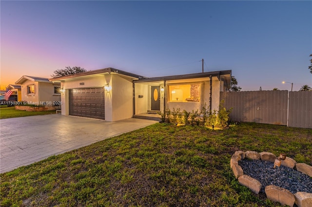 view of front of house featuring decorative driveway, stucco siding, an attached garage, a front yard, and fence