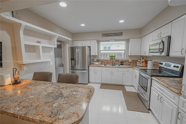 kitchen featuring light stone counters, appliances with stainless steel finishes, a sink, and white cabinetry