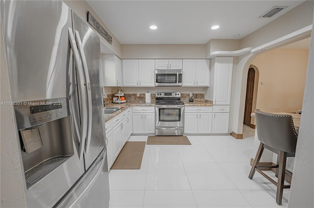 kitchen with visible vents, white cabinets, arched walkways, light stone counters, and stainless steel appliances