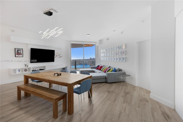 dining space featuring baseboards, light wood finished floors, an inviting chandelier, and floor to ceiling windows