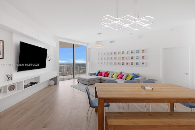 living area featuring visible vents, floor to ceiling windows, a notable chandelier, and light wood-style flooring