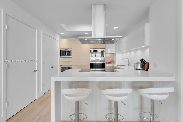 kitchen featuring modern cabinets, a breakfast bar area, a peninsula, island exhaust hood, and light countertops