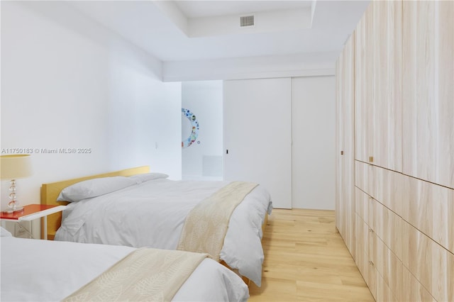 bedroom with light wood-style floors, a tray ceiling, a closet, and visible vents