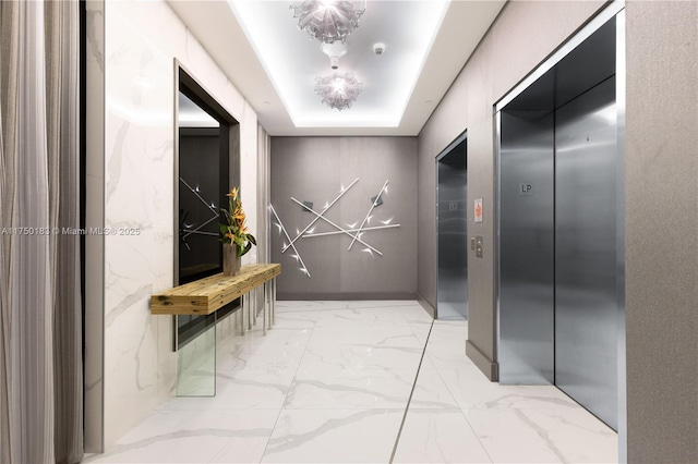 hallway with elevator, marble finish floor, and a tray ceiling