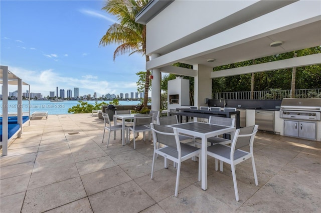 view of patio with a city view, a water view, an outdoor kitchen, outdoor dining space, and a grill