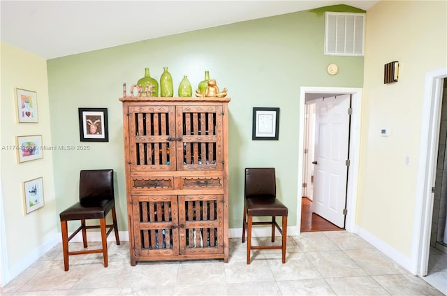 sitting room featuring vaulted ceiling, light tile patterned flooring, visible vents, and baseboards