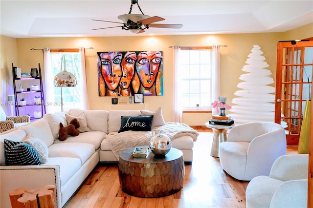 living room with light wood-style floors, a raised ceiling, and a ceiling fan