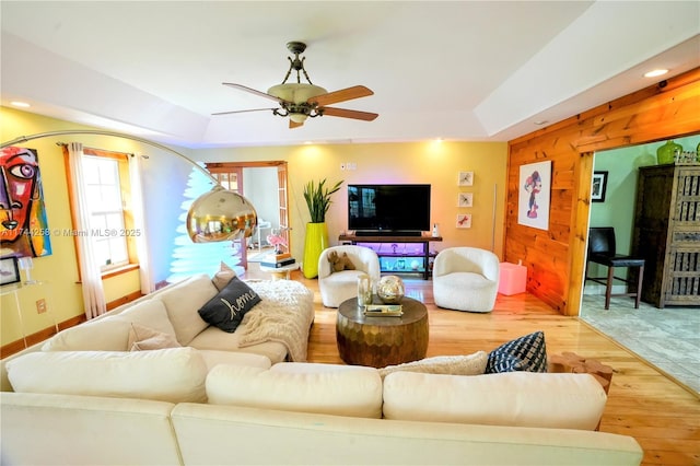 living area featuring recessed lighting, a raised ceiling, a ceiling fan, wood walls, and wood finished floors