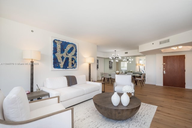 living room featuring visible vents, a notable chandelier, baseboards, and wood finished floors