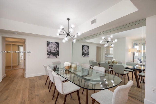 dining room with light wood-style floors, baseboards, visible vents, and a notable chandelier