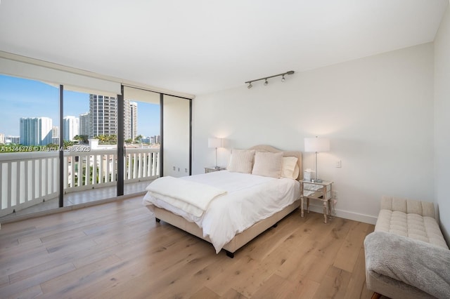 bedroom featuring a city view, baseboards, access to outside, light wood-type flooring, and floor to ceiling windows