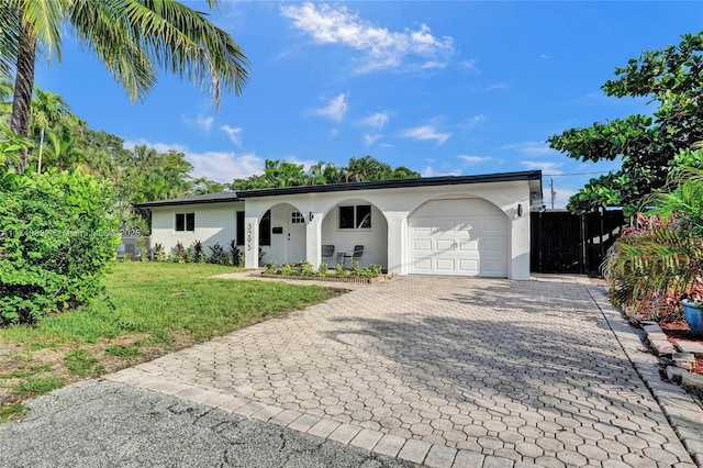 ranch-style house with a garage, fence, decorative driveway, a front lawn, and stucco siding