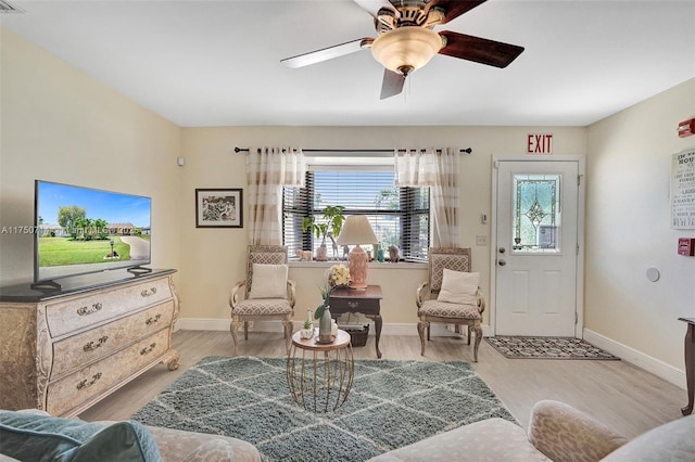 living room featuring a ceiling fan, baseboards, and light wood finished floors