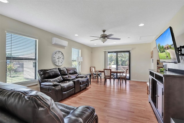 living area with a textured ceiling, ceiling fan, baseboards, light wood-style floors, and a wall mounted air conditioner