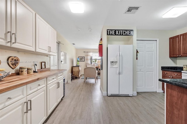 kitchen with white refrigerator with ice dispenser, visible vents, wooden counters, light wood-style floors, and white cabinets