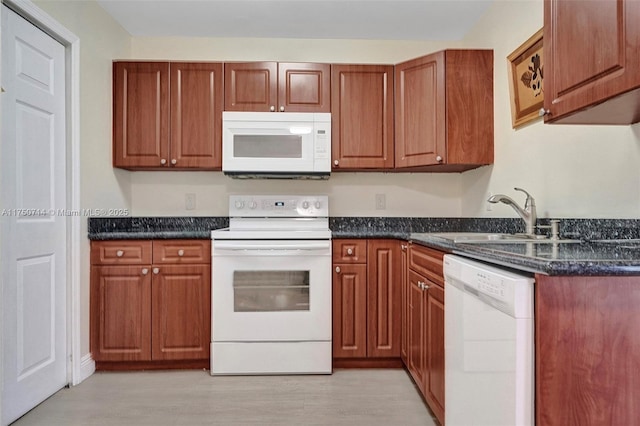 kitchen featuring white appliances, dark stone counters, brown cabinets, light wood-style floors, and a sink