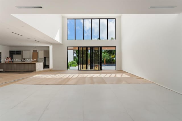 unfurnished living room with visible vents, a towering ceiling, and light tile patterned floors