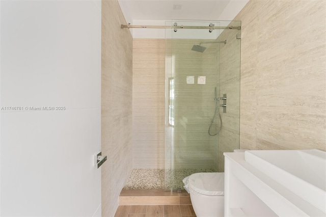 bathroom with tile walls, toilet, a sink, a shower stall, and wood finished floors