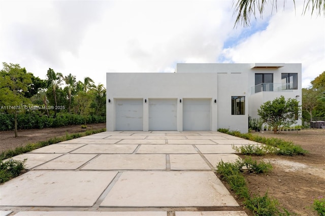 contemporary home with concrete driveway, a balcony, an attached garage, and stucco siding