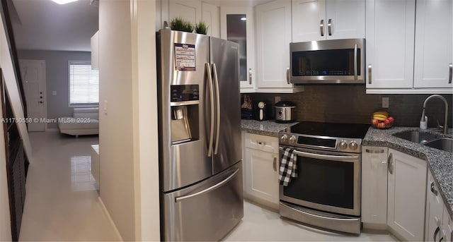 kitchen with stainless steel appliances, a sink, white cabinetry, dark stone counters, and tasteful backsplash