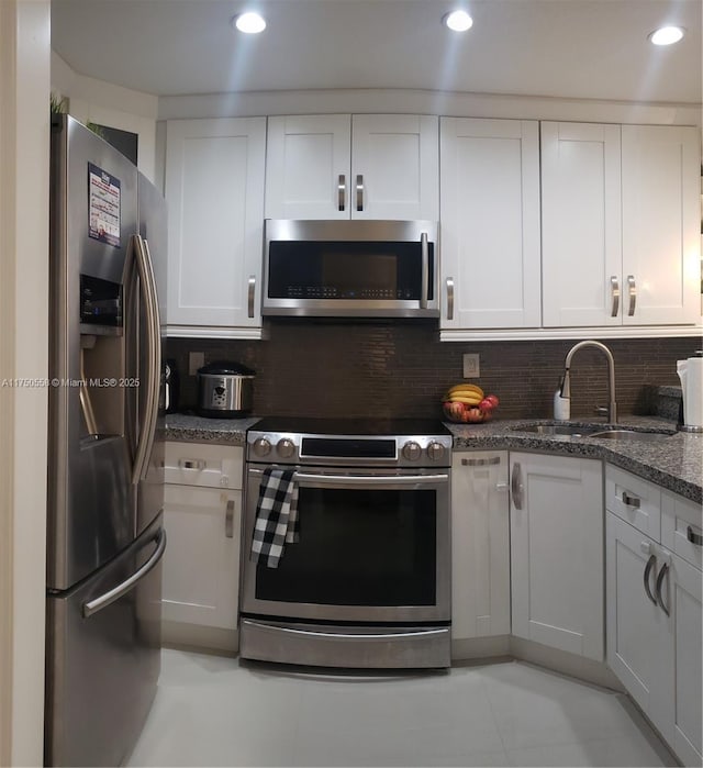 kitchen featuring white cabinets, appliances with stainless steel finishes, dark stone countertops, a sink, and backsplash