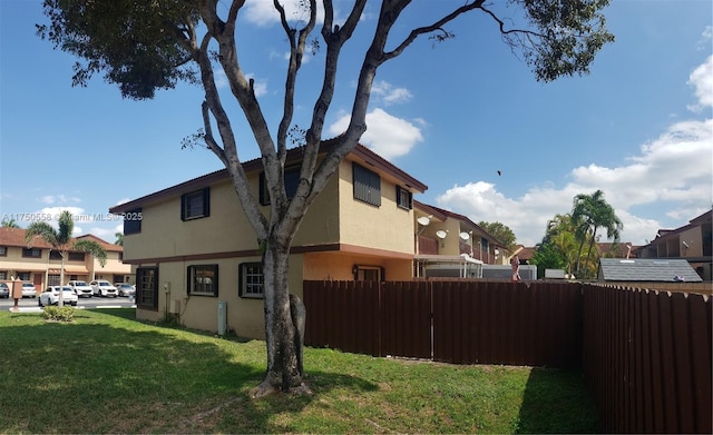 view of side of home featuring a residential view, stucco siding, fence, and a lawn