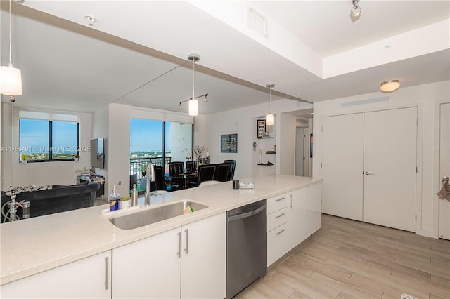 kitchen featuring white cabinets, dishwasher, light countertops, pendant lighting, and a sink