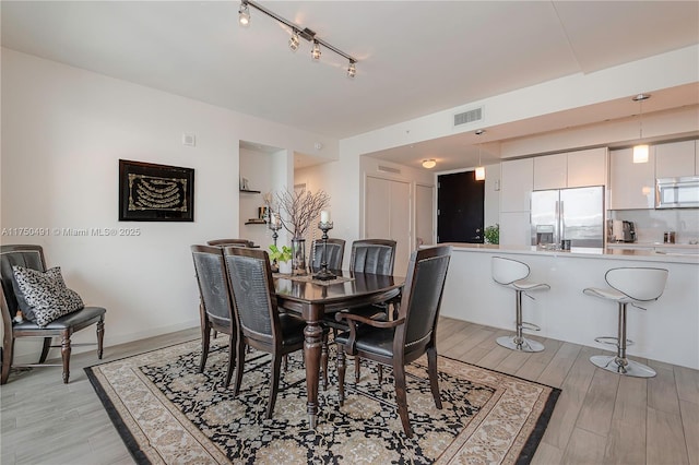 dining area with baseboards, light wood-type flooring, visible vents, and track lighting