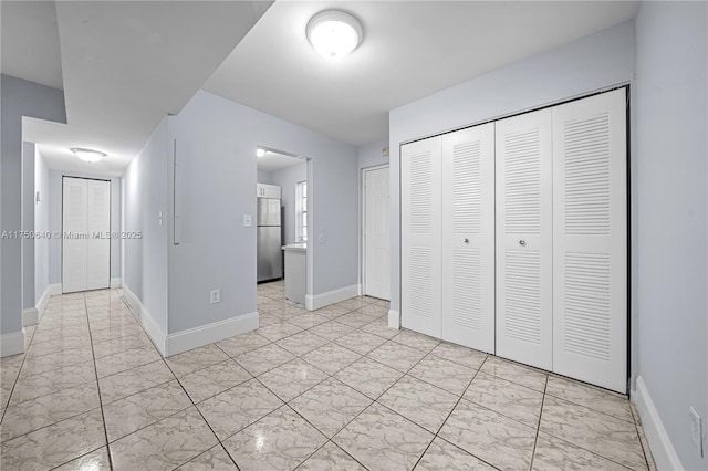 unfurnished bedroom with a closet, ensuite bathroom, baseboards, and stainless steel refrigerator