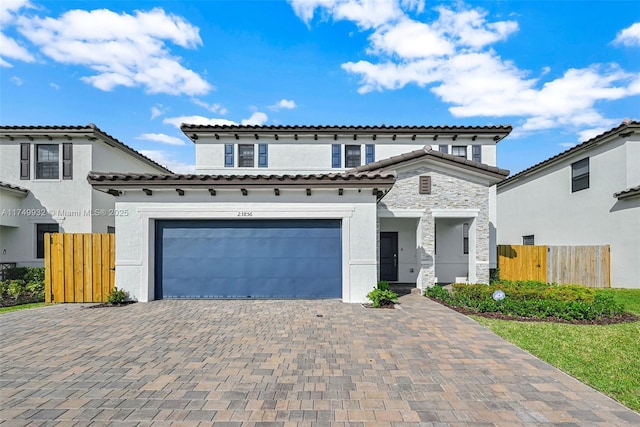 mediterranean / spanish home with stone siding, an attached garage, fence, and stucco siding