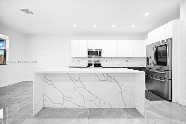 kitchen featuring stainless steel appliances, white cabinets, visible vents, and an island with sink