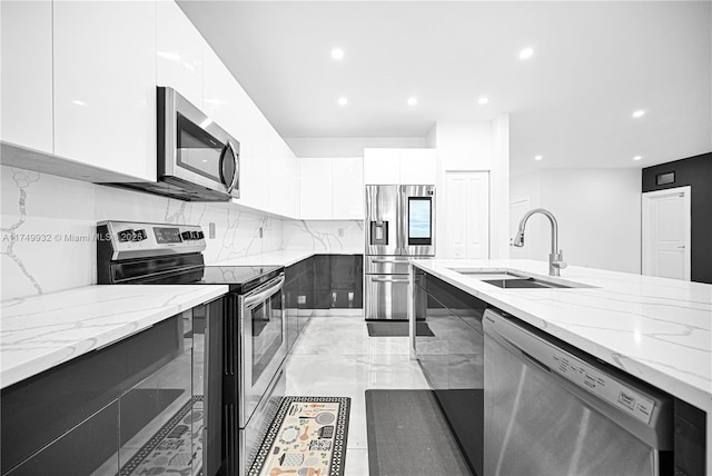 kitchen featuring white cabinets, modern cabinets, light stone counters, stainless steel appliances, and a sink