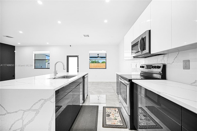 kitchen with stainless steel appliances, a sink, visible vents, light stone countertops, and modern cabinets