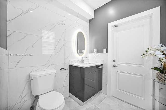 half bathroom featuring tile walls, marble finish floor, vanity, and toilet