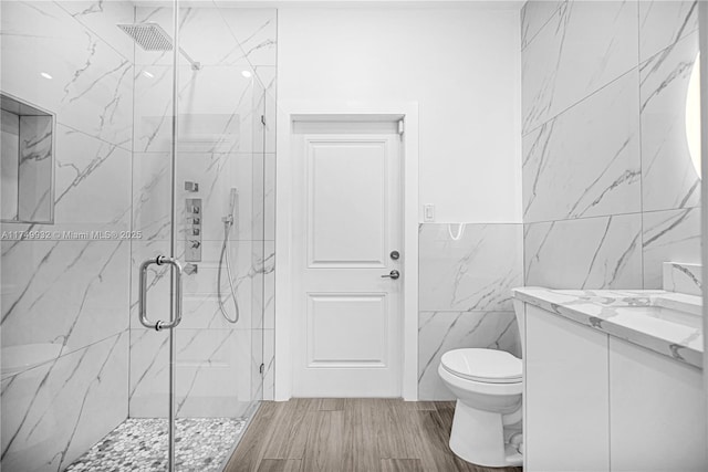 bathroom featuring tile walls, a marble finish shower, toilet, vanity, and wood finished floors