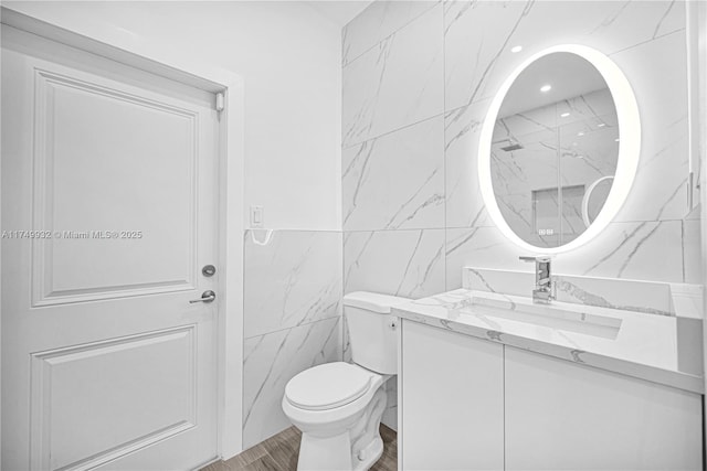 bathroom with wood finished floors, tile walls, toilet, and vanity