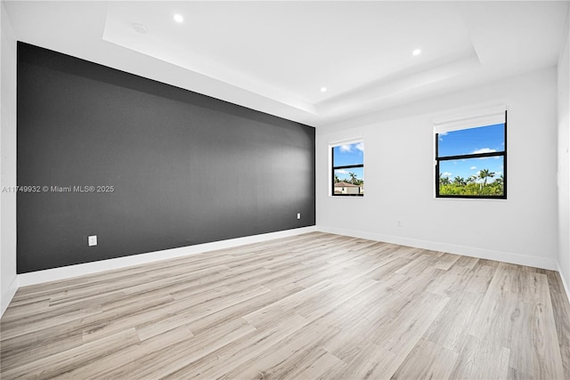 unfurnished room with a tray ceiling, light wood finished floors, baseboards, and recessed lighting