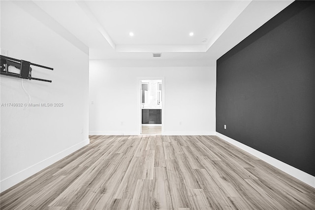 empty room featuring visible vents, baseboards, a raised ceiling, light wood-style flooring, and recessed lighting